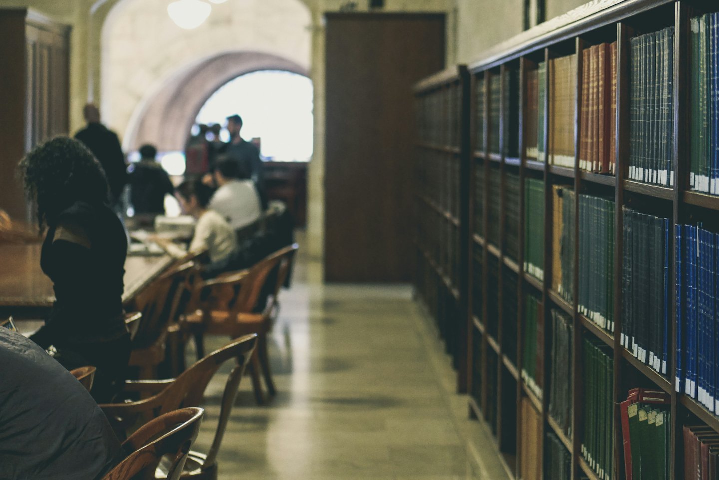 People studying at long tables in a bright library.